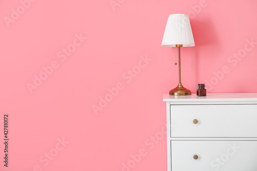 Modern chest of drawers and lamp near color wall in room