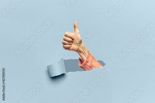 Woman hand appearing through a torn cardboard with the OK gesture photo