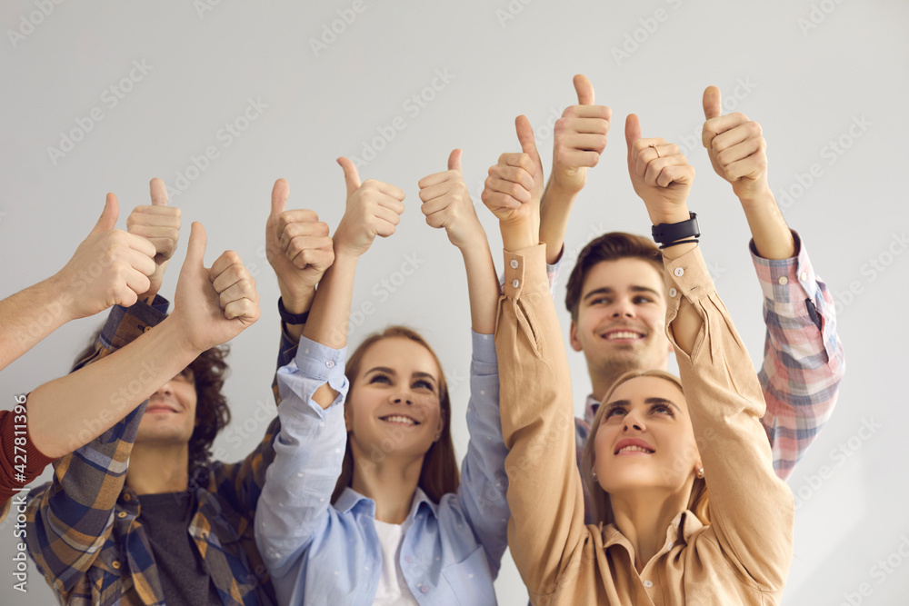 Team of smiling young people raising hands in air and giving thumbs-up. Group of happy motivated aspiring men and women doing like gesture all together. Student community, teamwork and success concept Team of smiling young people raising hands in air and giving thumbs-up. Group of happy motivated aspiring men and women doing like gesture all together. Student community, teamwork and success concept