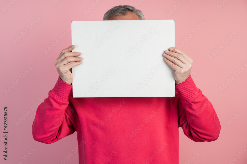 Man covers his face with a white sheet of paper. On a pink background copy space, place for text, advertising.