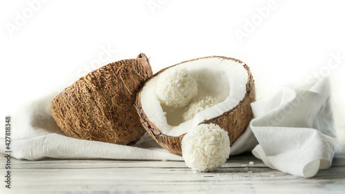Two halves of coconut and coconut sweets on a wooden table .  Coconuts on a white napkin . Handmade coconut sweets with a copy space  .  Horizontal orientation picture with a coconut .