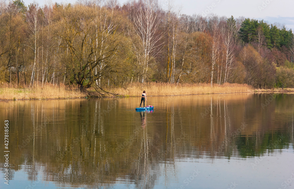 Warm colors in early spring by the lake with a view of nature. Lonely girl on a canoe goes in for sports