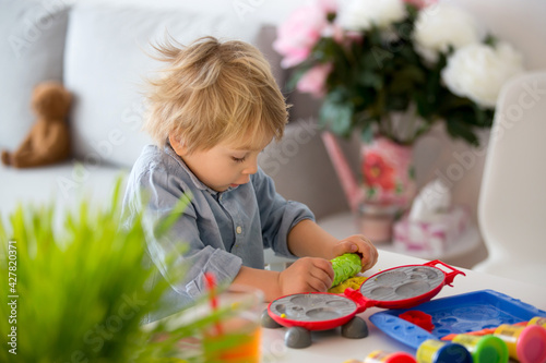 Cute blond child, boy, playing with play doh modeline at home, making different objects photo