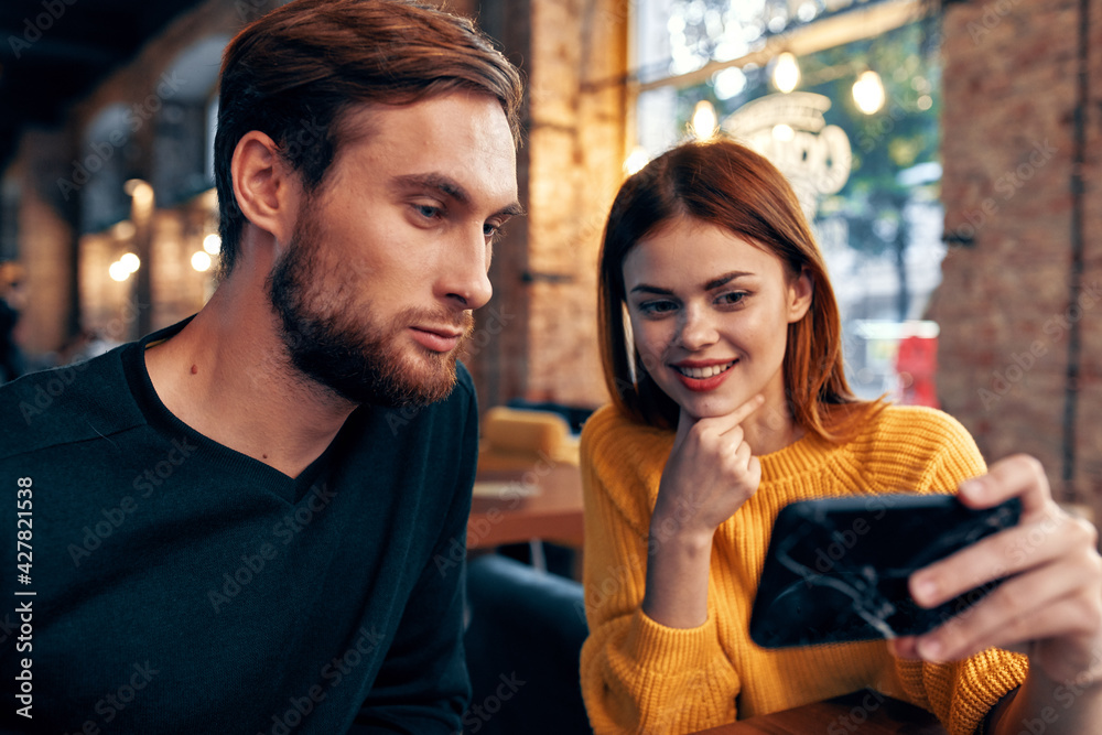 a woman in a sweater with a mobile phone and a guy with a beard are sitting in a restaurant a woman in a sweater with a mobile phone and a guy with a beard are sitting in a restaurant