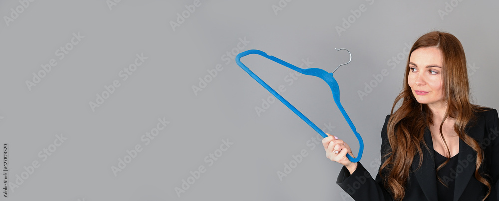 A frustrated woman holds a hanger for clothes on gray banner background. Doesn't have clothes or money to buy new dress A frustrated woman holds a hanger for clothes on gray banner background. Doesn't have clothes or money to buy new dress