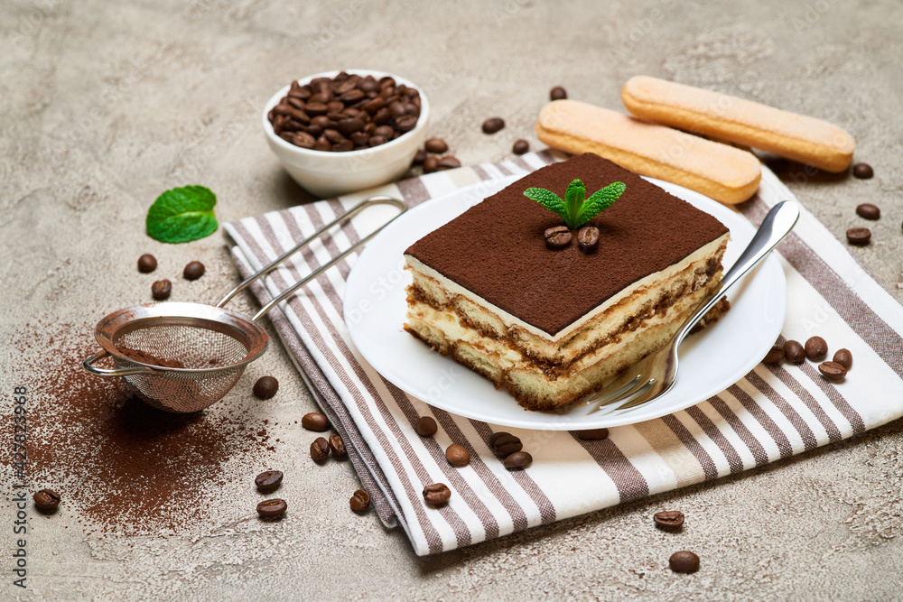 Portion of Traditional Italian Tiramisu dessert and coffee beans on grey concrete background Portion of Traditional Italian Tiramisu dessert and coffee beans on grey concrete background