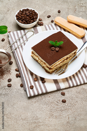 Portion of Traditional Italian Tiramisu dessert and coffee beans on grey concrete background