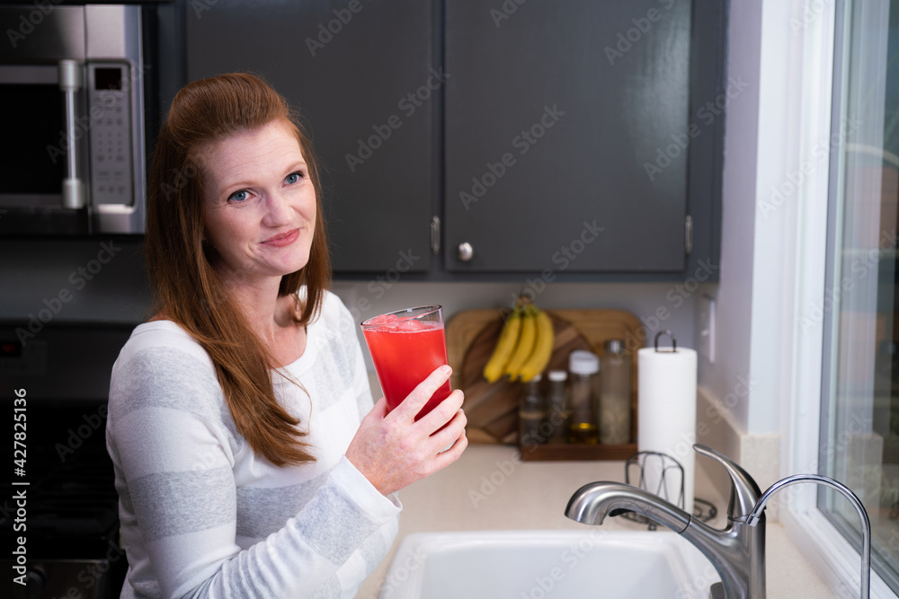 Red Head Caucasian Woman Mother Mom in Kitchen Looking at Blended Red Health Drink Ingredients Smiling Happy and Thoughtful Red Head Caucasian Woman Mother Mom in Kitchen Looking at Blended Red Health Drink Ingredients Smiling Happy and Thoughtful