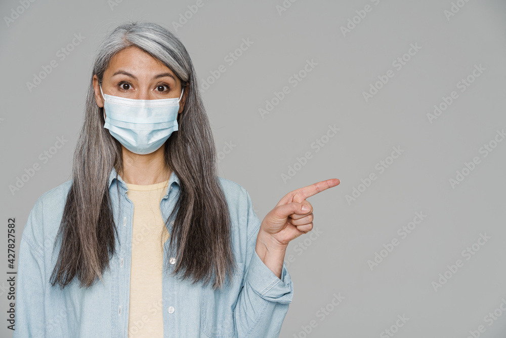 Mature white-haired woman in face mask pointing finger aside Mature white-haired woman in face mask pointing finger aside