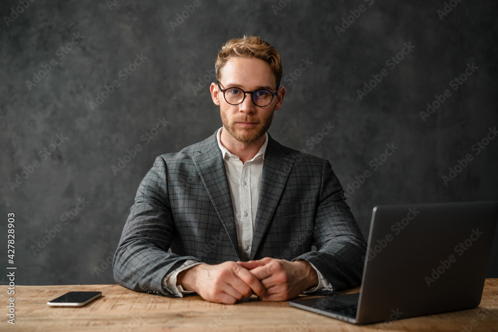 A man sitting at a table in front of a laptop and looking at the camera A man sitting at a table in front of a laptop and looking at the camera