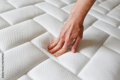 Cropped shot of young woman's hand testing white orthopedic mattress on firmness. Female pressing hypoallergenic foam mattress surface to check its softness. Close up, copy space, top view, background photo