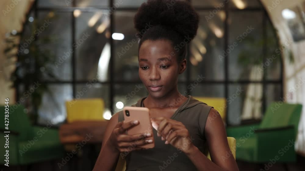 Close up view of millennial afro american woman looking amazed while using smartphone in cafe. Young female person scrolling social media news feed and showing emotions. Close up view of millennial afro american woman looking amazed while using smartphone in cafe. Young female person scrolling social media news feed and showing emotions.