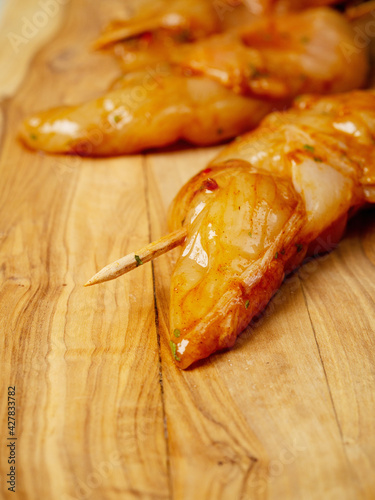 Marinated raw chicken pieces on a wooden skewer and wooden board and table. Summer barbeque range product. Asian style sous over poultry meat.