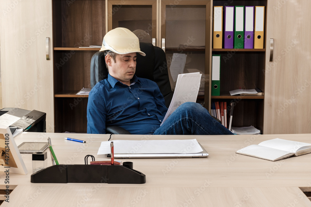 Serious boss in hard is reading an important document at the table. Conclusion of a contract. Builder, engineer, proctor, foreman. Serious boss in hard is reading an important document at the table. Conclusion of a contract. Builder, engineer, proctor, foreman.