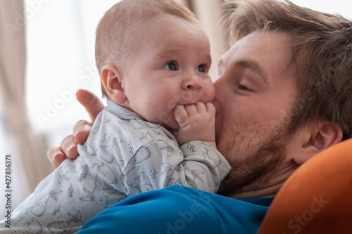 Sweet little infant lyes on his father’s torso and puts his fingers into the mouth. photo