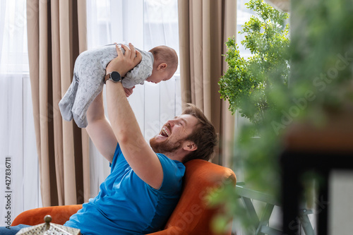 Fotografia Young father laughing at playing with his little son by uplifting him in the air