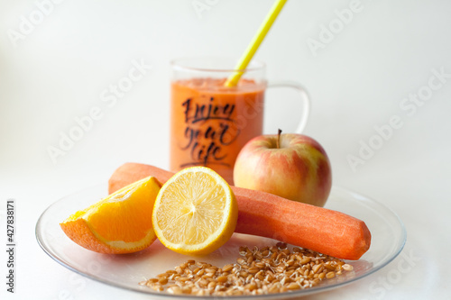 Orange smoothie made from healthy vegetables and fruits in a beautiful transparent mug on a white background. Healthy lifestyle. Contains carrot, orange, lemon, apple, wheat germ. Enjoy your life