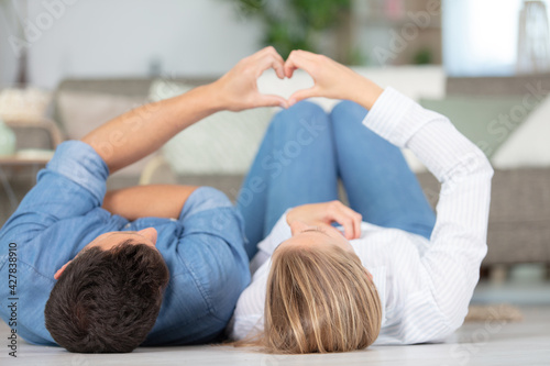 couple laying on the floor making heart sign with hands