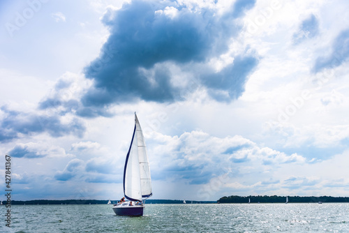 Yacht sailing on the lake against a blue sky with clouds. Sailboat vacations on a lake.