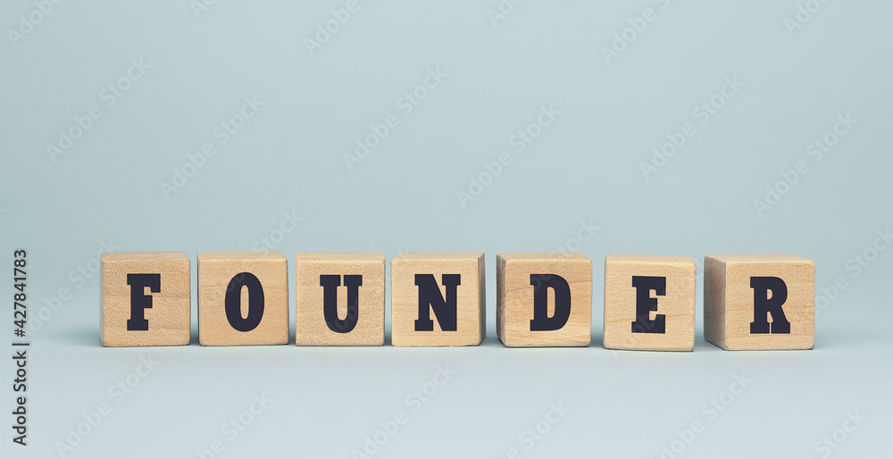 The word FOUNDER made from wooden cubes on blue background The word FOUNDER made from wooden cubes on blue background