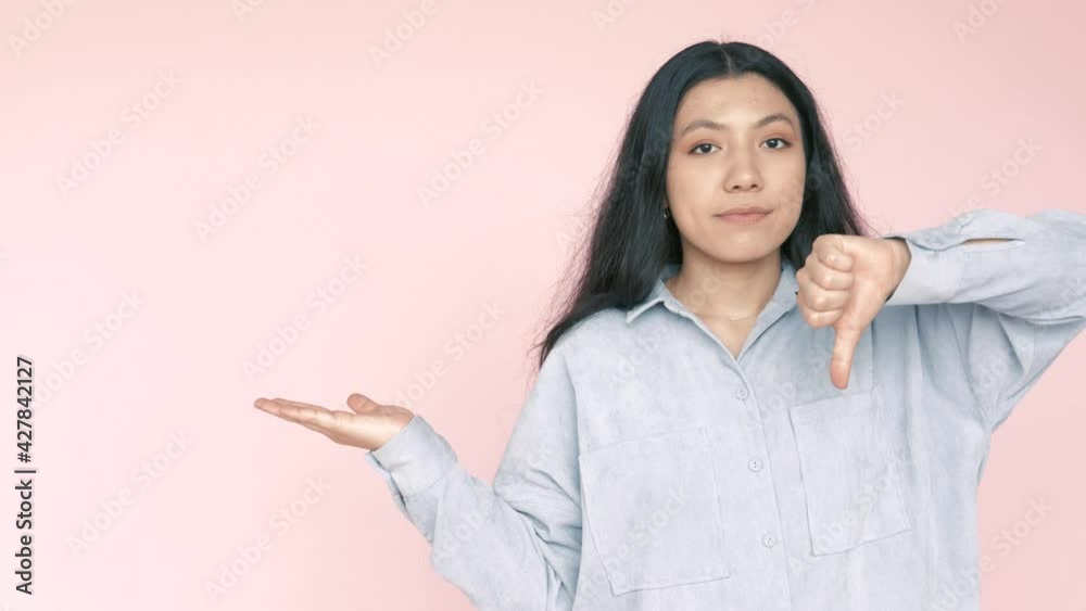 Look, advertise here! Smiling positive brunette hispanic woman pointing finger away at empty background, freespace for advertisement, thumb down, dislike. Indoor studio shot isolated pink background Look, advertise here! Smiling positive brunette hispanic woman pointing finger away at empty background, freespace for advertisement, thumb down, dislike. Indoor studio shot isolated pink background