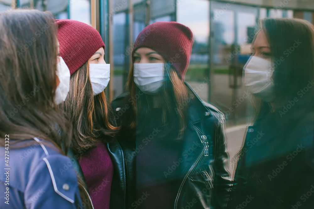 Close-up portrait of girls with medical masks. Against the background of a glass building with reflections. Concept on the topic of viros.