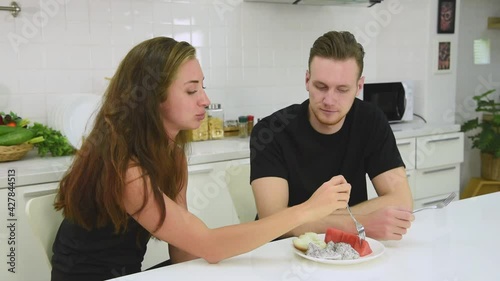 Man and woman couple in casual outfit eating healthy mix fruit food on white dish with fork for self care in modern kitchen