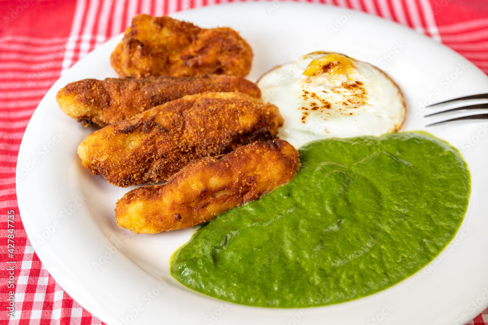 Spinach sauce, fried potato croquettes and fried egg on plate.