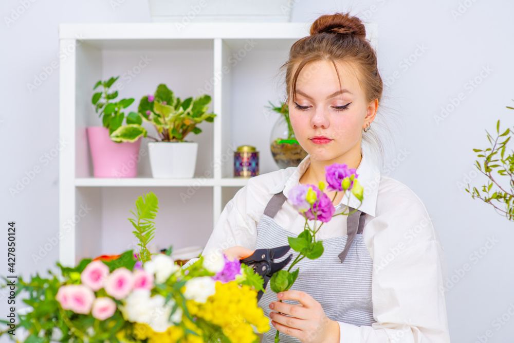 Cute girl florist collects a bouquet in a flower shop. A beautiful florist creates a composition of flowers. Girl cuts flowers and removes stale leaves. Cute girl florist collects a bouquet in a flower shop. A beautiful florist creates a composition of flowers. Girl cuts flowers and removes stale leaves.