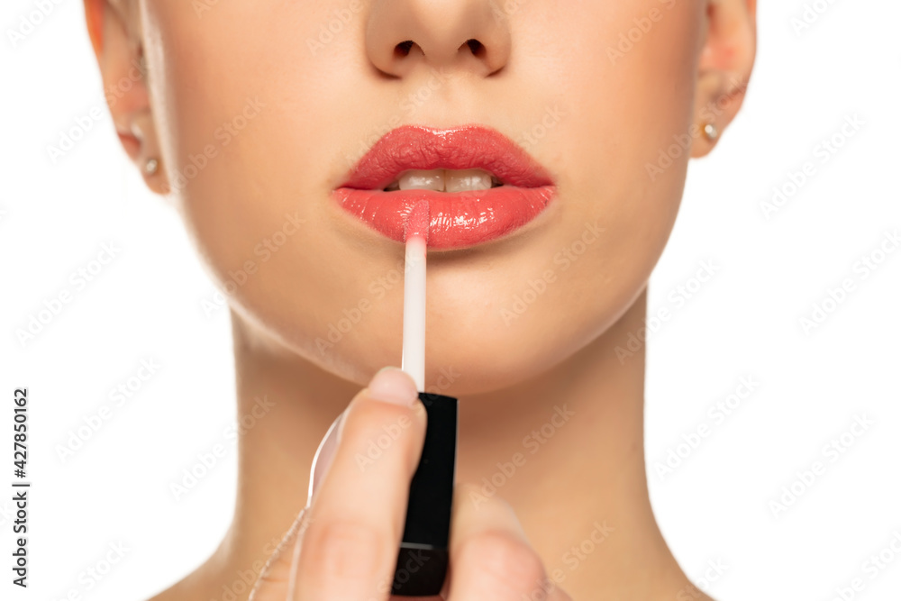 Closeup of woman applying a lip gloss on her lips on a white background Closeup of woman applying a lip gloss on her lips on a white background