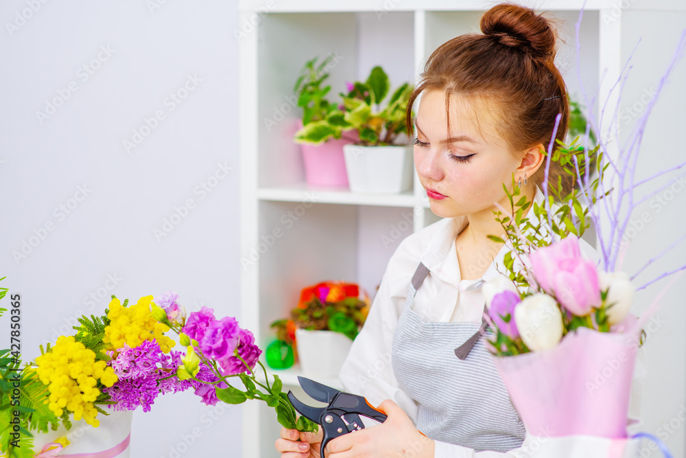 Cute girl florist collects a bouquet in a flower shop. A beautiful florist creates a composition of flowers. Girl cuts flowers and removes stale leaves.