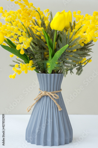 A gray vase with tulips and mimosa on the table. Easter decor. Spring concept