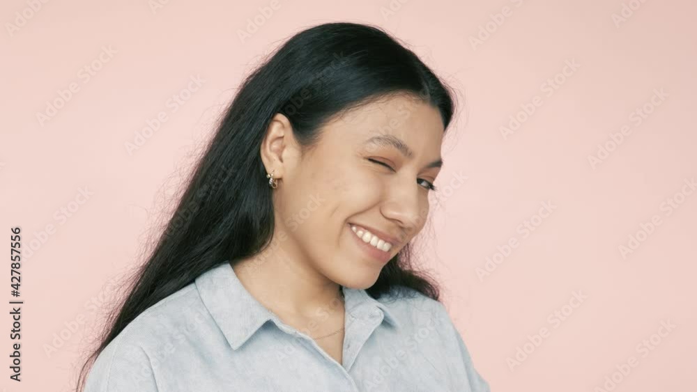Friendly happy positive latin hispanic woman looking at camera with toothy wide smile and blinking winking, flirting, saying hello. Indoor studio shot isolated on pink background Friendly happy positive latin hispanic woman looking at camera with toothy wide smile and blinking winking, flirting, saying hello. Indoor studio shot isolated on pink background