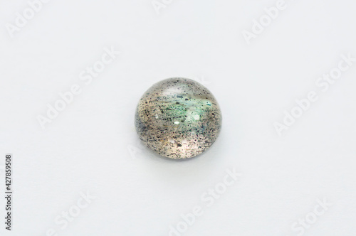 Natural labradorite round polished cabochon gemstone setting. Light green sheen  Inclusion of other dark flakes minerals in the crystal mass. Close-up macro photo on white background.
