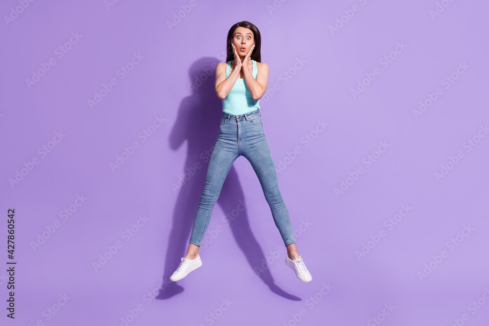 Full length body size photo of brunette jumping up touching cheeks staring amazed isolated on pastel purple color background Full length body size photo of brunette jumping up touching cheeks staring amazed isolated on pastel purple color background