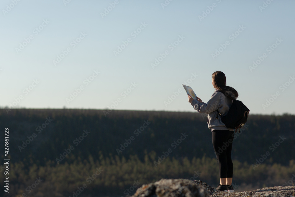 A young lady traveler with backpack standing on the rocky mountain and explore route a paper map. A young lady traveler with backpack standing on the rocky mountain and explore route a paper map.