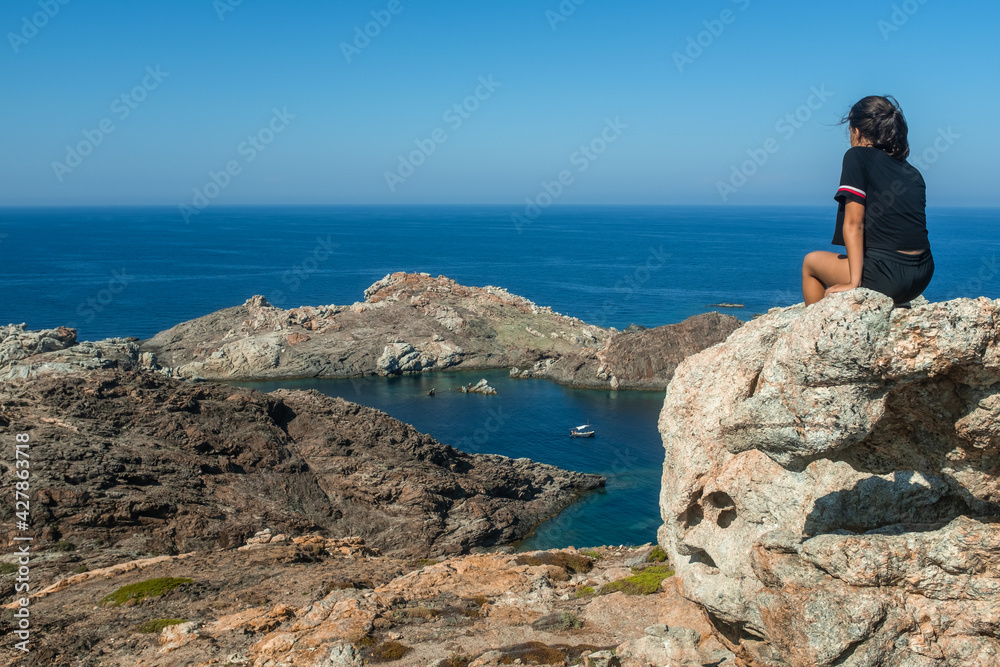 Thoughtful teenage girl looking at sea on a sunny day, Cap de Creus (Cape of Crosses), Catalonia, Spain.