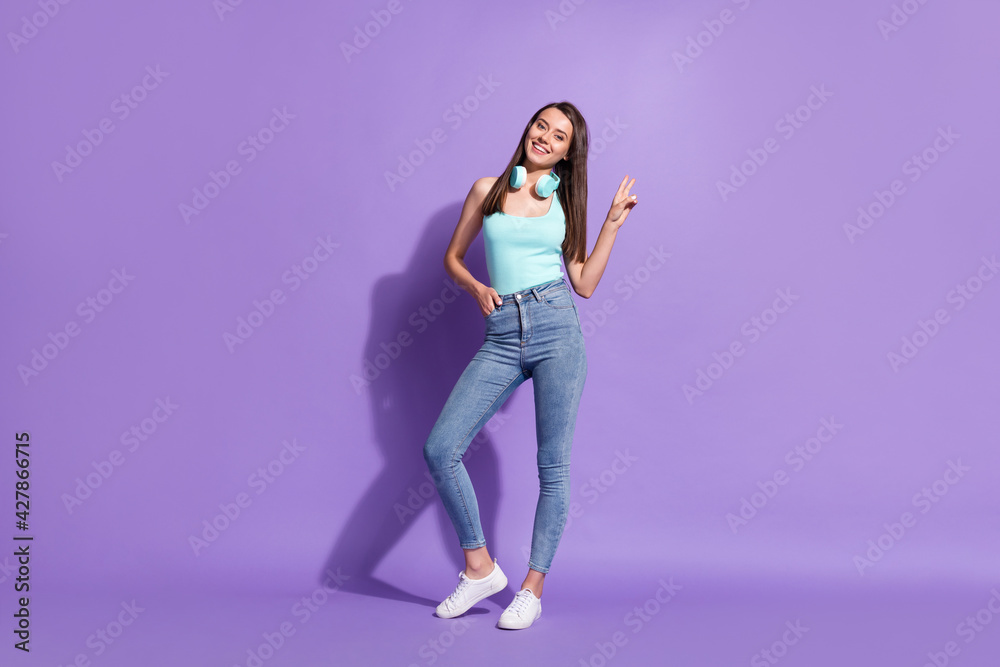 Full length body size photo of girl wearing headphones showing v-sign gesture smiling isolated on pastel violet color background