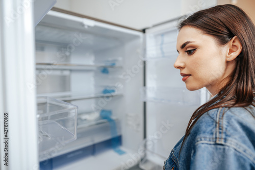 Young attractive woman choosing refrigerator in hypermarket
