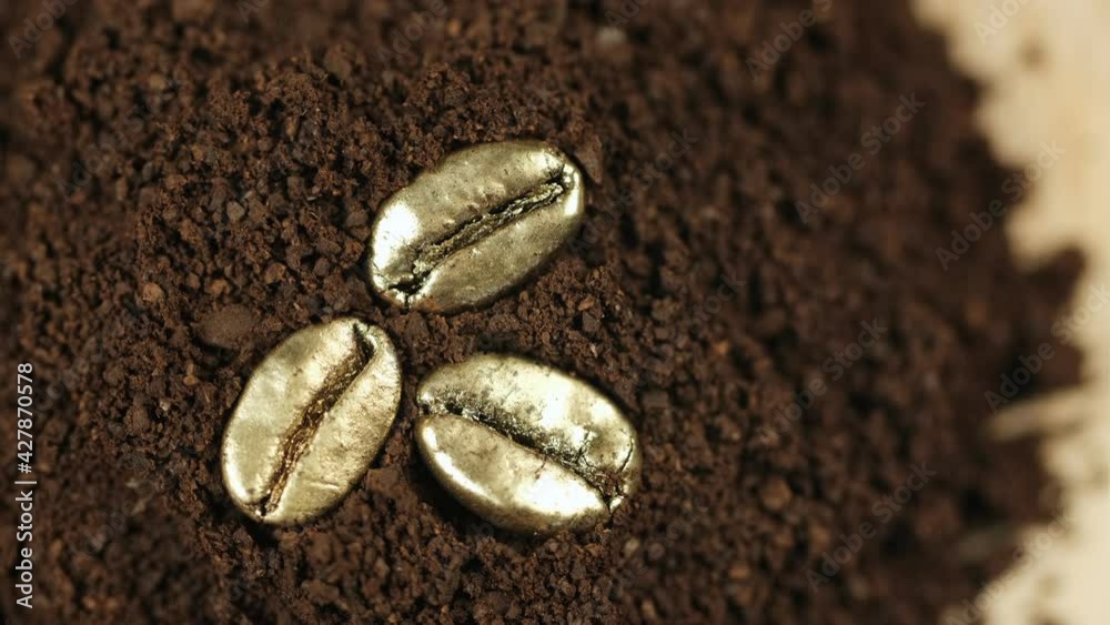 Golden coffee beans. Three roasted gold coffee beans lie on the ground coffee and slowly rotate. 4K Golden coffee beans. Three roasted gold coffee beans lie on the ground coffee and slowly rotate. 4K