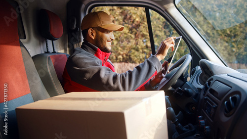 Delivery driver looking at tablet and then outside to confirm delivery address. High quality photo