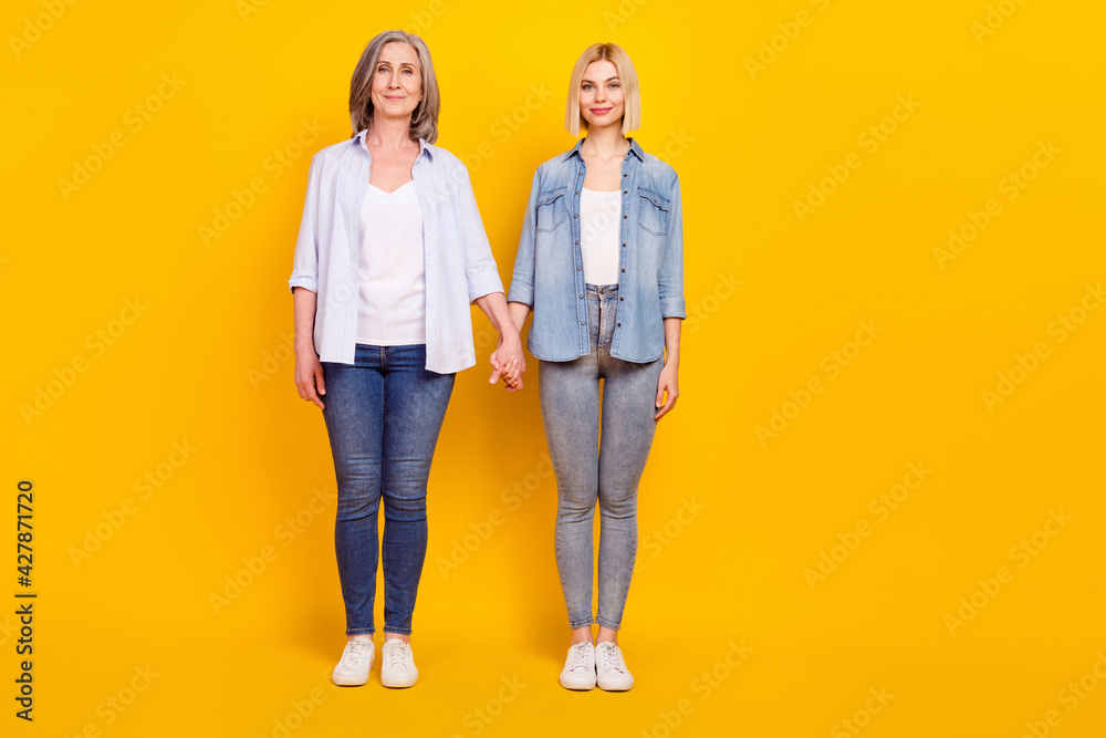 Full length body size photo of granddaughter and granny wearing casual clothes holding hands isolated vibrant yellow color background