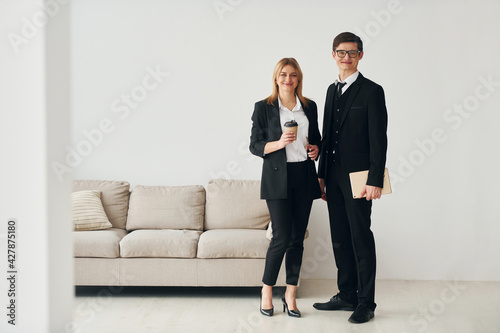 Young guys standing with woman indoors near sofa agaist white wall © standret