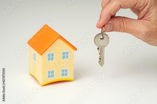 Toy house and male hand holding keys isolated on white background. Concept of real estate agent handing over the keys of the house to the new owner.