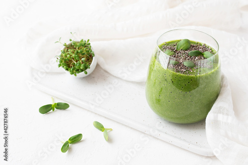 Raw green smoothie with microgreens alfalfa sprouts and chia seeds in a glass on a cutting board and white tablecloth