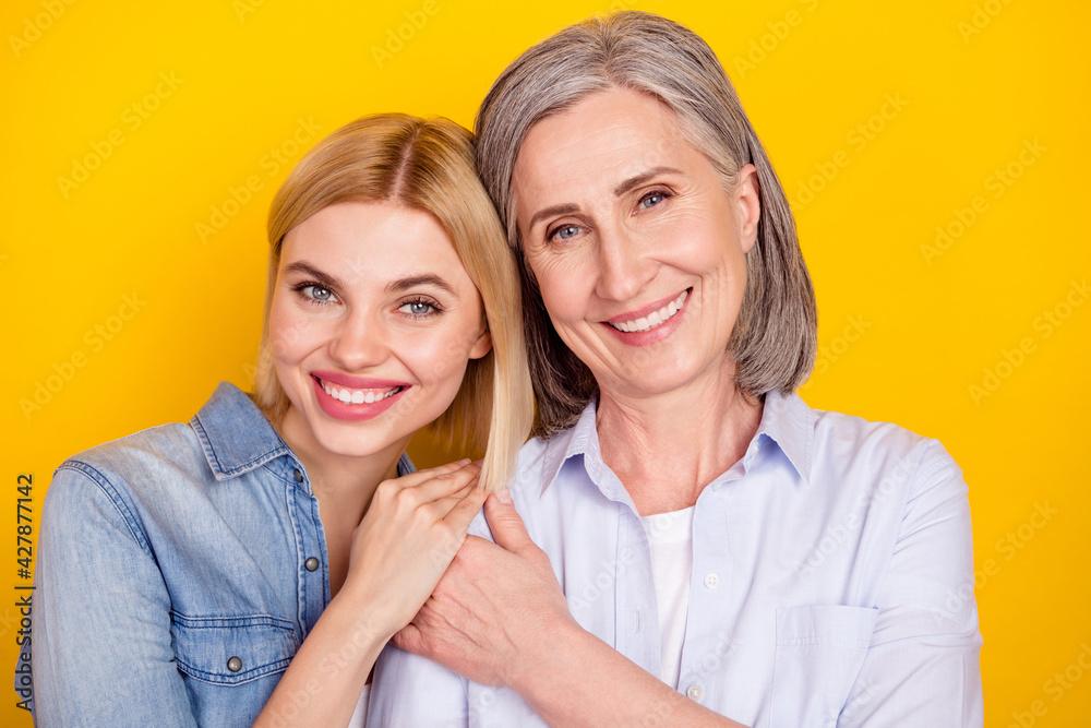 Photo portrait of daughter and mother smiling holding hands together isolated vibrant yellow color background