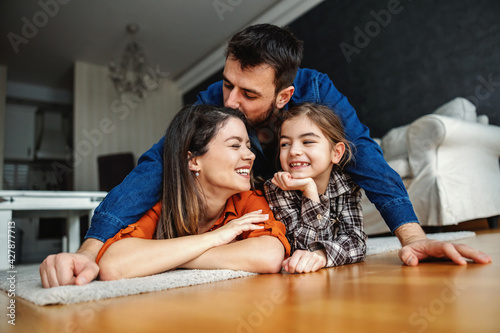 Happy family having great time together. Mom and daughter lying on the floor while dad kissing mom. healthy childhood.