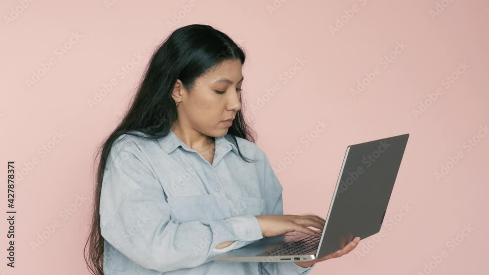 Clever positive hispanic beautiful girl holding laptop and typing, chatting with friends in social networks, leaves comments. Indoor studio shot isolated on pink background Clever positive hispanic beautiful girl holding laptop and typing, chatting with friends in social networks, leaves comments. Indoor studio shot isolated on pink background