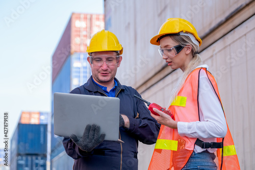 Two foreman and cargo container worker discuss together in workplace area with one hold and using laptop and the other hold walkie-talkie to contact their team.