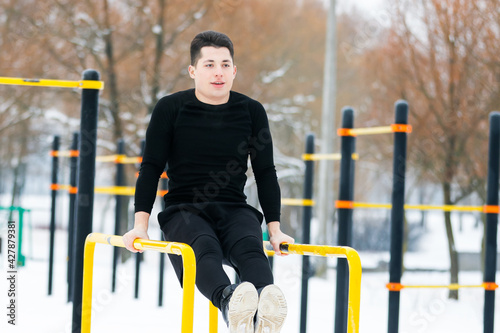 Fotografia A man does push-ups in winter during morning sports with the help of the yellow exercise machine